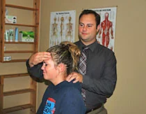 Man performing cranial adjustment on child's head in medical office with anatomical charts on wall
